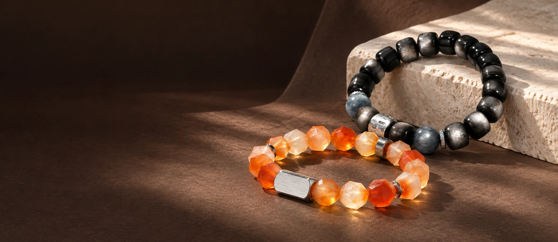 Dark obsidian and orange agate bracelets on a sculptural chocolate brown surface